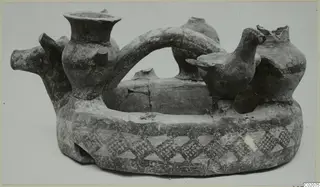 Pottery vessel with a ring-shaped base, painted triangle bands, a modelled bird and an animal head, photographed against a pale background
