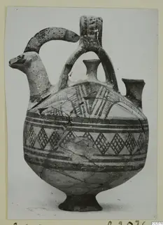 White Painted I jug with an animal-head spout, a second small spout and a looped handle, decorated with painted bands and hatched patterns.
