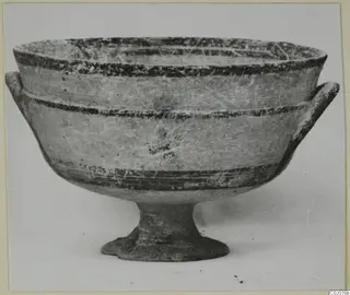 Pottery bowl on a stemmed foot with two horizontal handles, dark painted bands on a pale surface