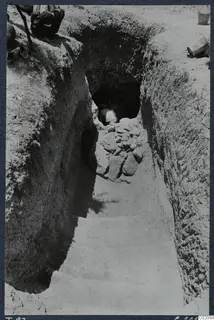 Sloping dromos leading down to a tomb entrance at Marion, with a person in the doorway and a bucket on the bank.