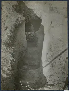 Steps leading down a narrow rock-cut passage at Marion to a tomb opening blocked by stones, with a vessel on top.