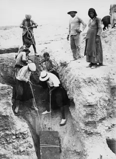 Workers pulling ropes to haul a wooden board up a narrow trench at Marion, with a man and woman watching from the edge.