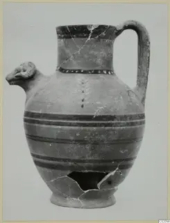 Pottery jug with a modelled animal-head spout and a strap handle, photographed against a plain background.