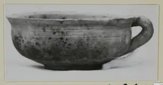 Pottery bowl with a single loop handle and a small foot, shown in profile against a white background