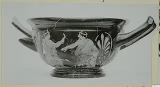 Two-handled skyphos with two painted figures and a palmette ornament, photographed on a mount.