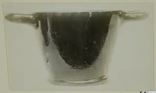 Black glazed pottery bowl with two horizontal handles and a low ring foot, seen from the side.