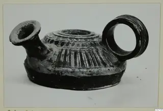Pottery oil lamp with a short spout, ring handle and striped shoulder, shown on a pale background