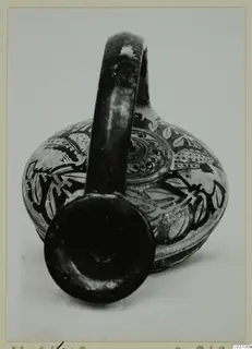 Painted pottery vessel with a loop handle and dark leaf and scroll decoration, mouth turned toward the camera.