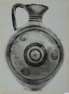 Black-on-red jug with a single handle, a ring-and-spiral decorated body and a flaring mouth, shown against a plain background.