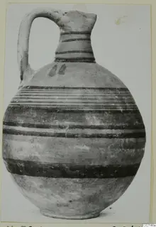 Jug with a strap handle and horizontal bands of dark paint, shown against a plain light background.