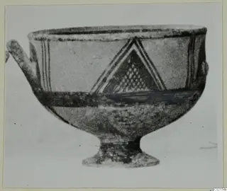 White Painted I bowl with a stemmed foot, one handle, and a triangular painted motif on the body.