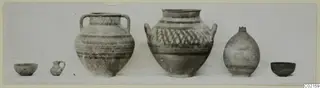 Six pottery vessels set in a row, including two large two-handled jars with painted bands and lattice decoration.
