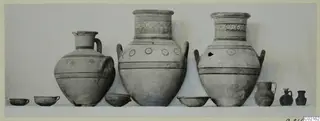 Group of pottery vessels from Tomb 77 at Marion, lined up on a shelf against a plain backdrop.