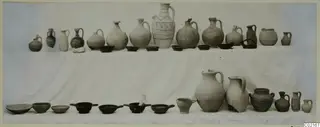 Pots and bowls from Tomb 25 at Marion, arranged in two rows on a white cloth.