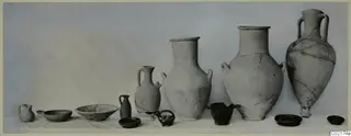 Row of pottery vessels from Marion, Tomb 45, including jugs and bowls, set out on a white cloth.
