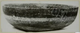 Side view of a rounded bowl with a wide open mouth, dark surface and a pale band around the body