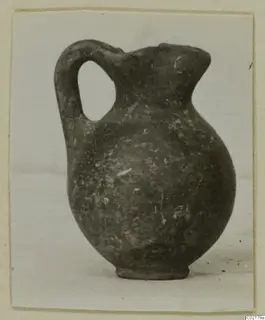 Black-on-Red jug with a single loop handle and ring base, photographed on a pale surface