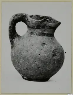 Small juglet with a loop handle and rounded body, photographed on a grey card mount