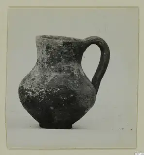 Pottery Red Slip jug with a single loop handle, photographed on a plain background