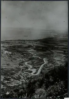Wide view over grassy hills and a coastal plain, with a winding road and a ship at sea