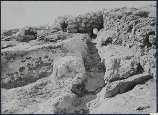 Excavated walls and loose stones at the palace at Vouni, with a narrow cut passage running between them.