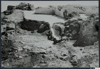 Excavated ruins at the palace at Vouni, with low pale walls and a sunken area in the centre.