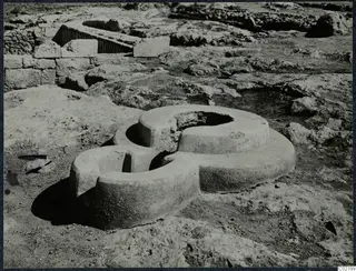 Two interlocking circular stone rings on bare rock at Vouni Palace, with stone walls behind