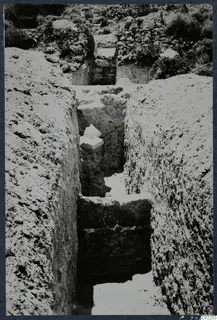 Narrow excavation trench at Vouni Palace with pale stones and objects lying on ledges in the cut