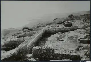 Excavated stone walls at Vouni Palace on a hilltop, with two people walking along the ridge at upper right