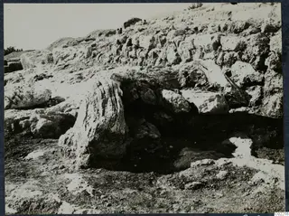 Large rock blocks and a rough stone wall on a slope at Vouni Palace, with small figures on the hillside above.