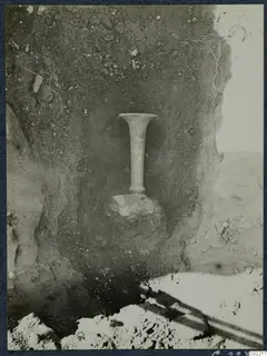 Tall stemmed vessel with a flared rim standing in soil at Vouni Palace, during excavation