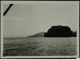 Dark rocky headland rising from the sea at Petra tou Limniti under a pale sky.