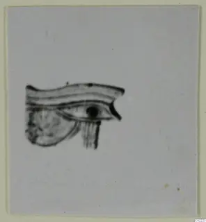 Blurred photograph of a small stylised eye-shaped motif with a curved brow band, mounted on a pale card.