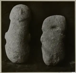 Two roughly shaped stone objects standing upright against a dark background, from Petra tou Limniti.