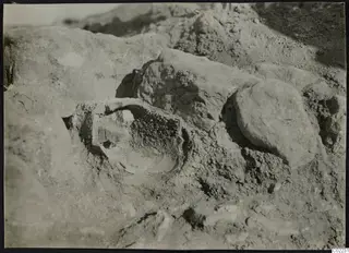 Excavated ground at Ayios Iakovos with a partly uncovered rounded object among stones and earth.