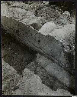 Excavation at Ayios Iakovos showing a cut face of layered soil with stones and a rounded pale object partly exposed