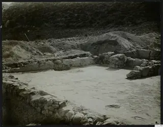 Excavated area at Ayios Iakovos with low stone walls around a pale floor surface.