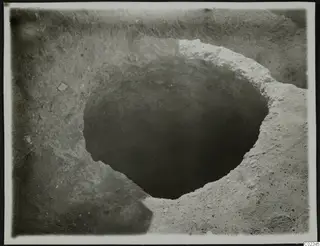 Round pit cut into excavated soil at Ayios Iakovos, with small stones scattered in the surrounding ground.