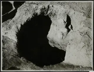 Dark round opening cut into pale earth at Ayios Iakovos, with white stones set in the soil beside it.