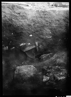 Vertical excavation section with a curved clay water channel set in the soil beside stone blocks