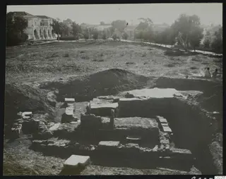 Excavated stone walls and foundations at the eastern part of Bamboula, with a building in the background