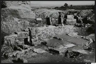 Excavated ruins of room 11 at Kition, with stone walls and paving in the foreground and a flat plain beyond.