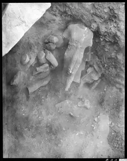 Excavated statue fragments in soil, with a large headless sculpture standing in the middle of the group