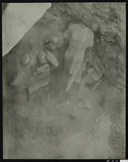 Statues and stone fragments lying in excavated soil at Kition, with a large headless sculpture in the middle.