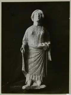 Limestone statuette from Vouni of a standing figure in a draped garment, holding a small dish at chest height.