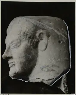Head of a sculpted figure in left-facing profile, in a pale material, on a dark background