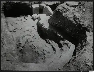 Excavated tomb at Amathus with scattered skeletal bones, small bowls and a pale rounded object during excavation.