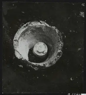 Round pale object with a raised central cylinder, seen from above in excavated soil at Amathus