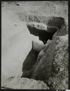 Excavation at Amathus: a sloping cut in pale soil leads to a dark opening, with a large fallen stone block in front of it