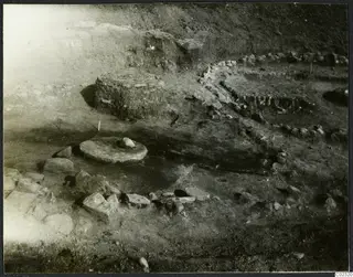 Excavation at Kythrea showing a stone construction: a round flat stone slab and low stone walls in the excavated ground.
